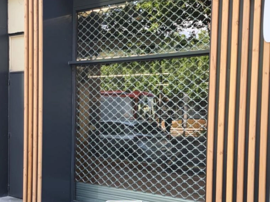 Grille de sécurité métallique à mailles sur devanture commerciale anthracite et bois, pose AFC à Caen.