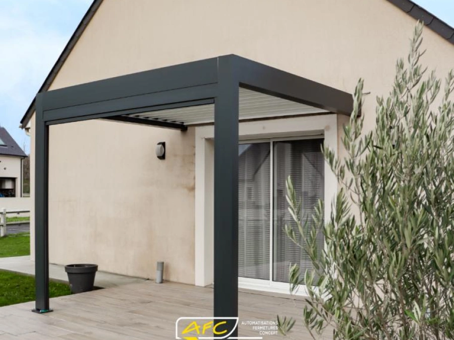 Pergola bioclimatique aluminium anthracite adossée à une maison, terrasse aspect bois et olivier, AFC Calvados.