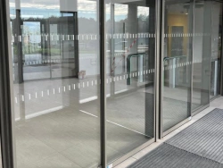 Portes automatiques coulissantes en verre vues depuis le hall, capteurs et tapis d'entrée, pose AFC Calvados.