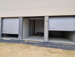 Portes industrielles sectionnelles grises mi-ouvertes sur box de stockage professionnels près de Caen