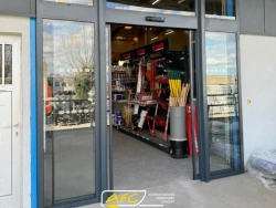 Porte automatique vitrée ouverte sur magasin de fournitures, menuiserie aluminium anthracite AFC