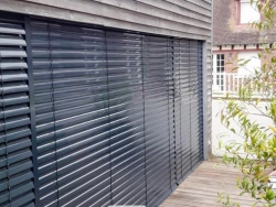 Brise-soleil orientable aluminium gris sur grande baie vitrée et terrasse bois, Normandie